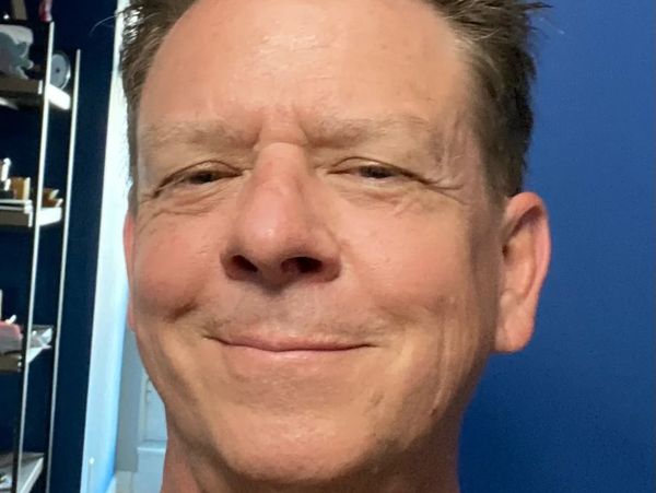 Smiling man with short hair in a room with blue walls.