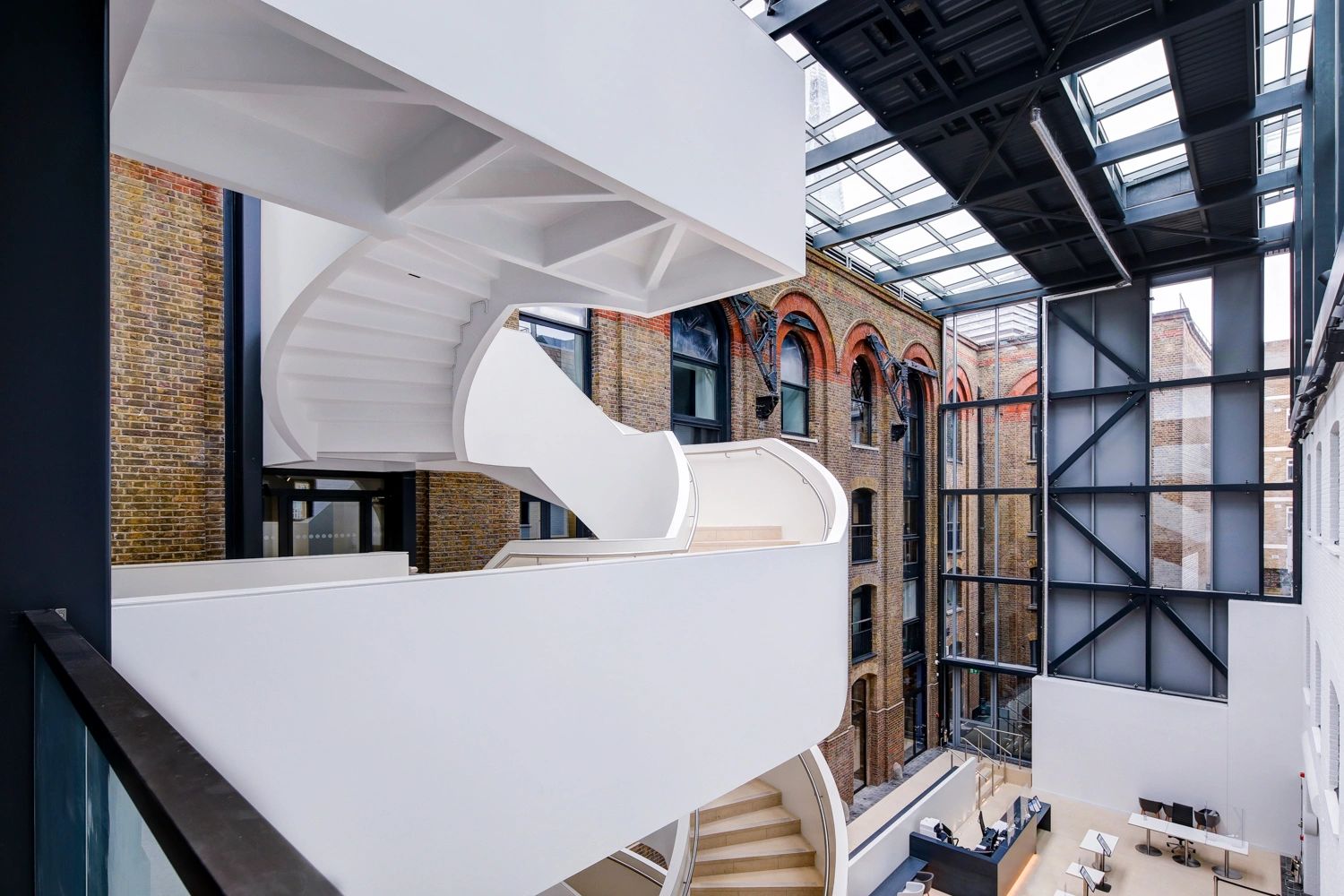 Modern white spiral staircase inside a building with exposed brick walls and large windows.