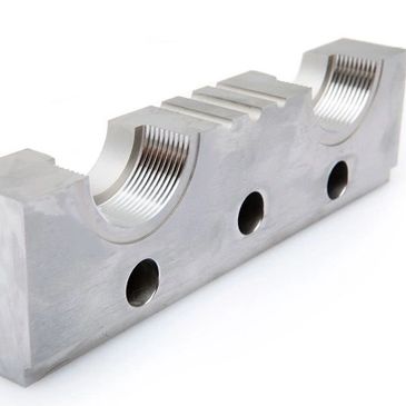 A silver metal block with two semicircular grooves and three holes.