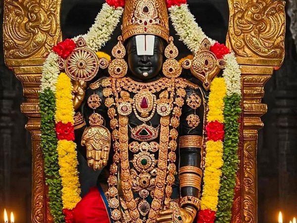 Ornate black deity statue adorned with gold jewelry and colorful flower garlands.