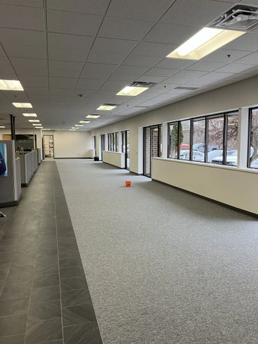 Empty office space with carpet and tile flooring and large windows along one wall.