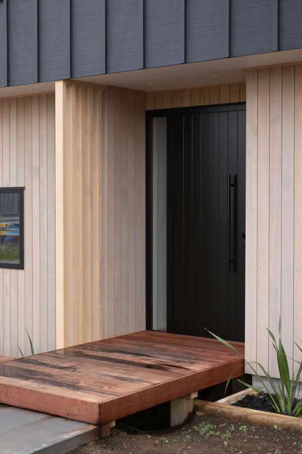 Modern entrance with wooden ramp and black door.