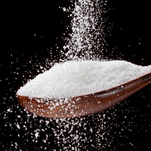 Granulated white sugar being poured into a wooden spoon against a black background.