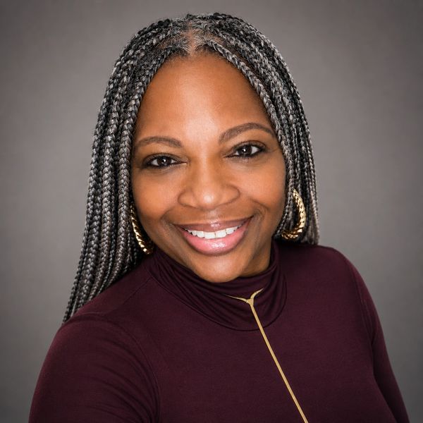 Smiling woman with braided hair and gold hoop earrings.