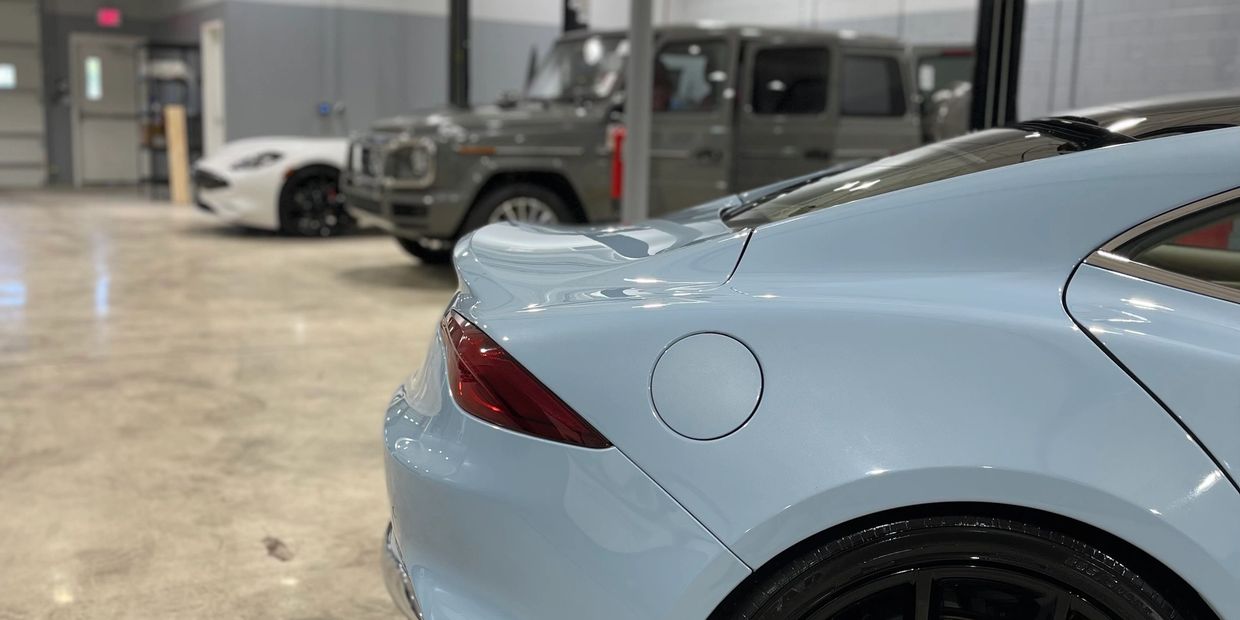 Light blue sports car rear with black wheels in a spacious garage.