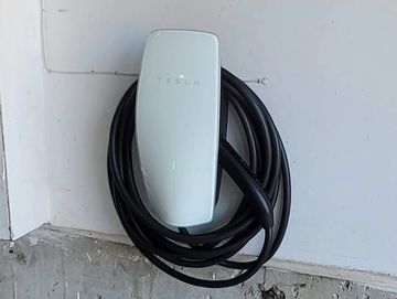 Tesla electric vehicle charger mounted on a garage wall with coiled charging cable.