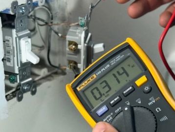Using a multimeter to measure voltage in a wall switch circuit.