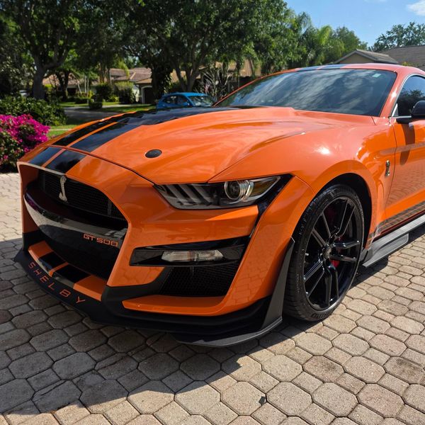 Orange Shelby GT500 Mustang parked on a driveway with black racing stripes.
