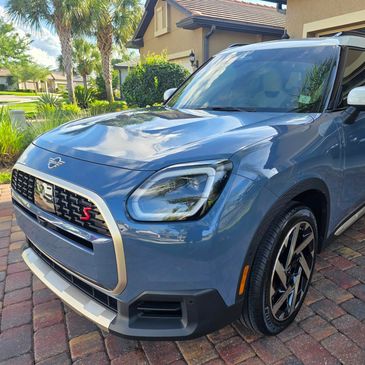 Blue Mini Cooper SUV parked on a brick driveway in front of a house.