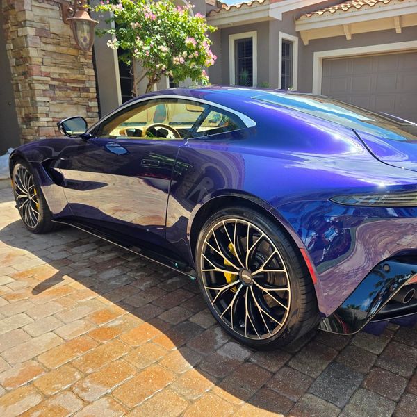 Sleek purple sports car parked on a cobblestone driveway.