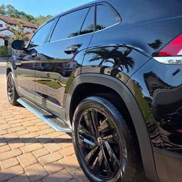 Shiny black Volkswagen SUV parked on a sunny driveway with palm trees reflected.