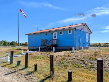 Blue coastal building with a windsock on a sunny day.