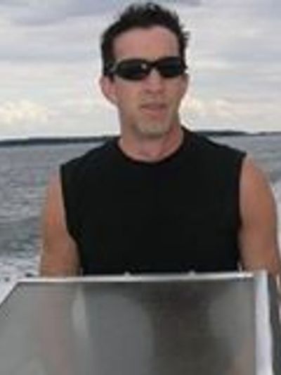 Man wearing sunglasses and sleeveless black shirt on a boat.