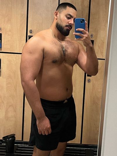 Man taking a shirtless mirror selfie in a locker room.