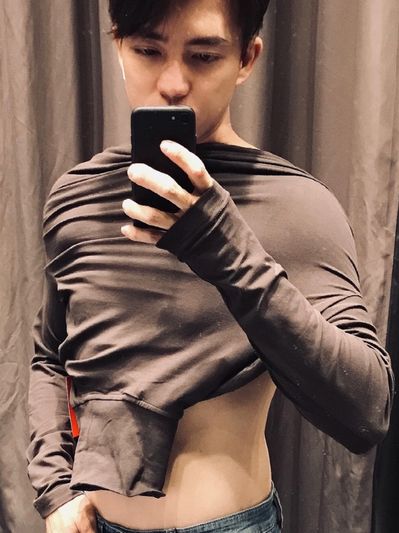 A young man taking a mirror selfie lifting his shirt.