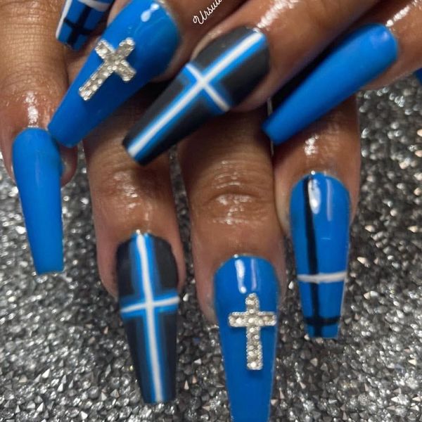 Blue coffin-shaped nails with cross designs and rhinestones.