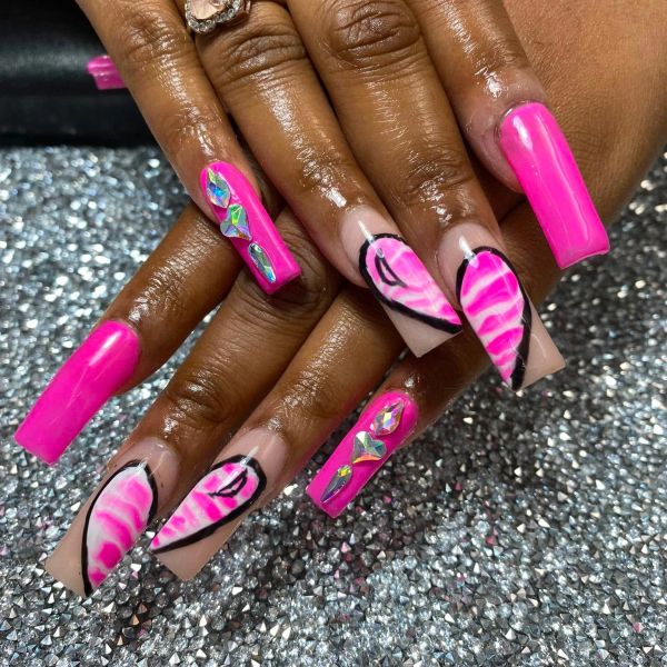 Long pink nails with heart designs and rhinestones.