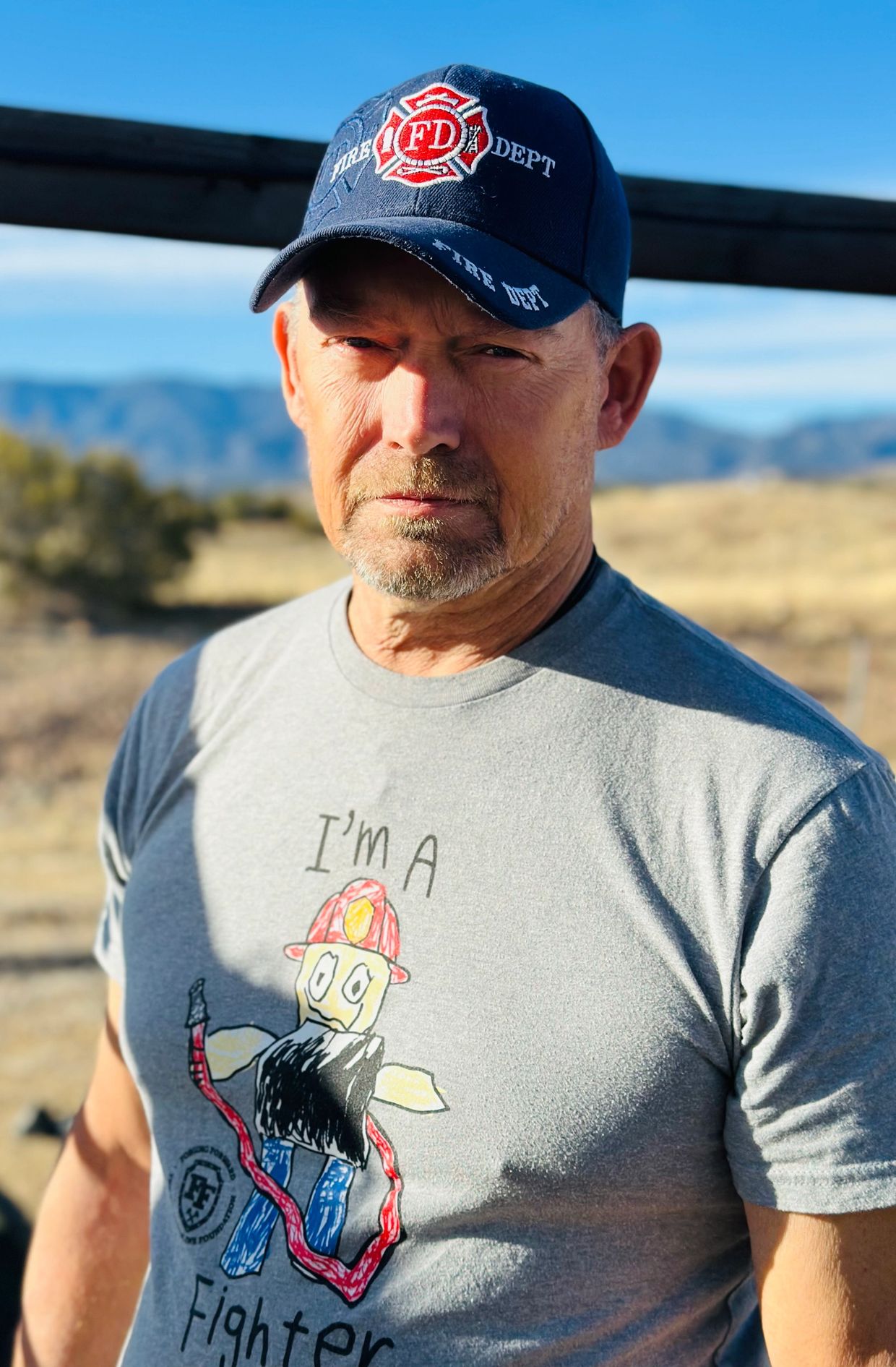Man wearing fire department hat and firefighter-themed shirt outdoors.
