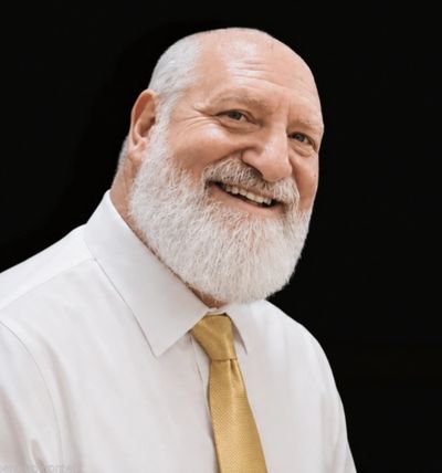 Smiling elderly man with white beard in white shirt and yellow tie.