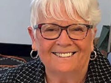 Elderly woman smiling with glasses and hoop earrings.