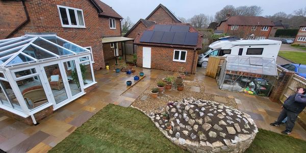 Backyard with conservatory, small greenhouse, and rock garden under cloudy sky.