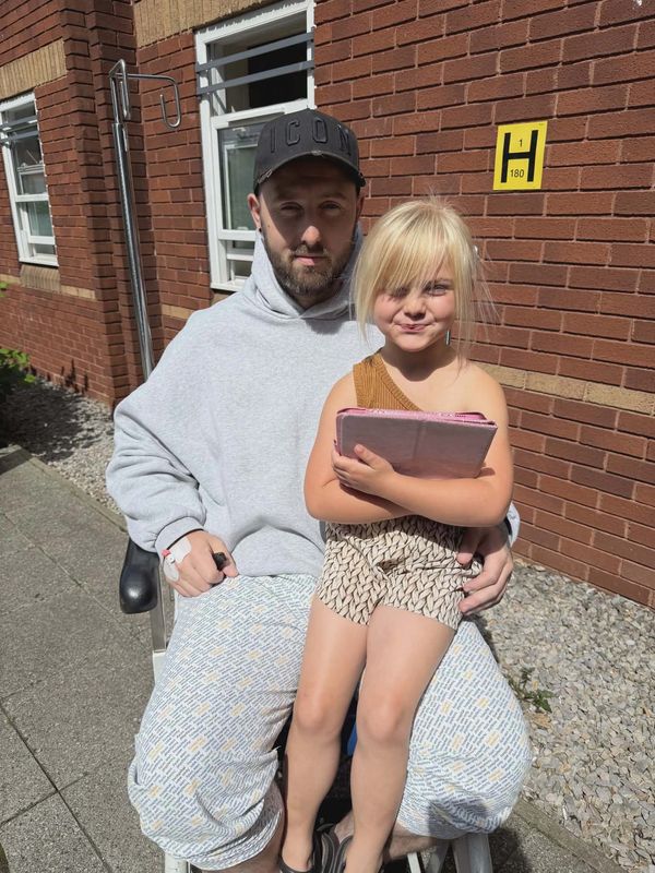 Man in wheelchair holding a young girl outside a brick building.