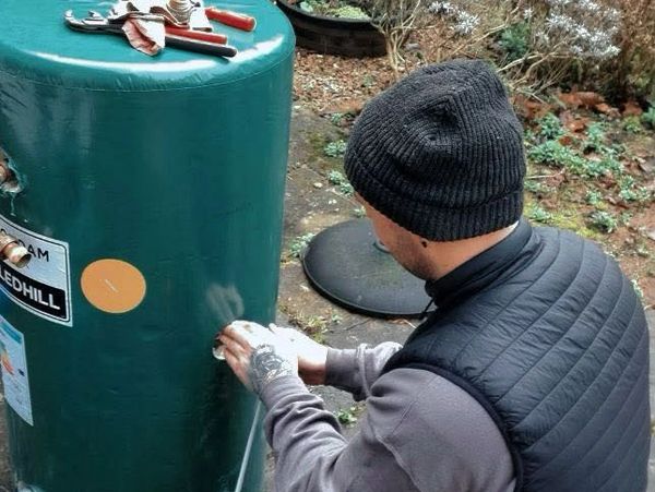 Man working on a green water heater outdoors with tools on top.