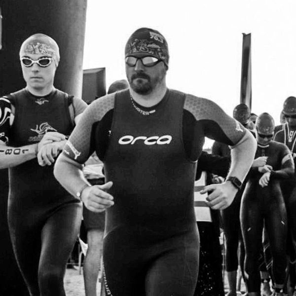 Swimmer in wetsuit, cap and goggles running down a beach. Lots of other swimmers behind.