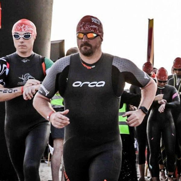 Swimmer in wetsuit, cap and goggles running down a beach. Lots of other swimmers behind.