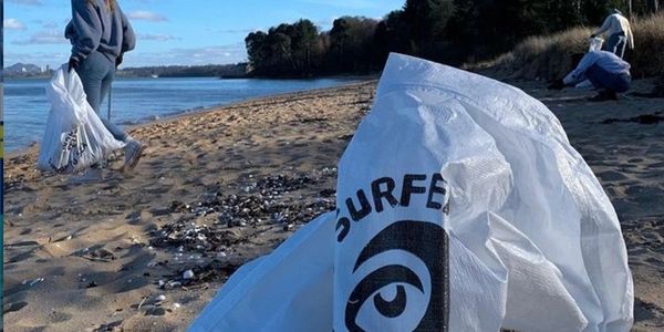 Surfers against sewage bag on beach with two people litter picking on a beach in the background.