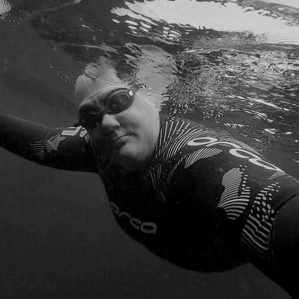Swimmer taken from underwater wearing a wetsuit, blue cap and goggles.