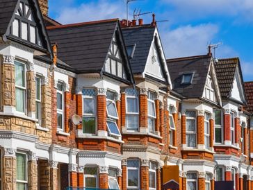 Row of traditional British terraced houses with bay windows and gabled roofs.