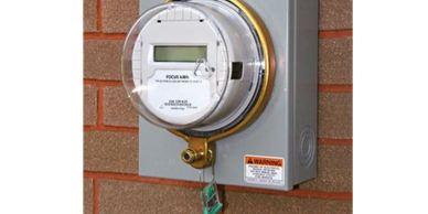 A digital electricity meter mounted on a brick wall.