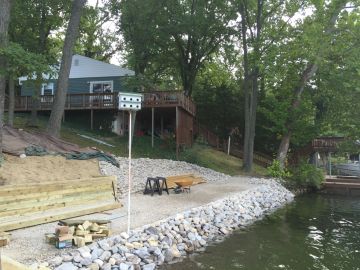 A lakeside house with a wooden deck and rocky shoreline.