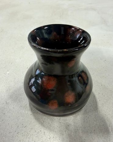 Glossy black ceramic vase with brown spots on a light surface.