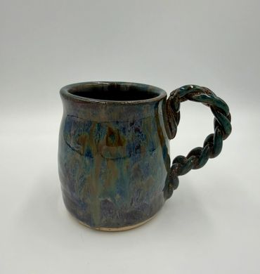Handcrafted ceramic mug with a twisted handle and a glossy, multicolored glaze.