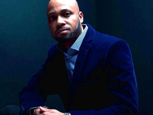 Confident man in a dark blue blazer poses against a dark background.