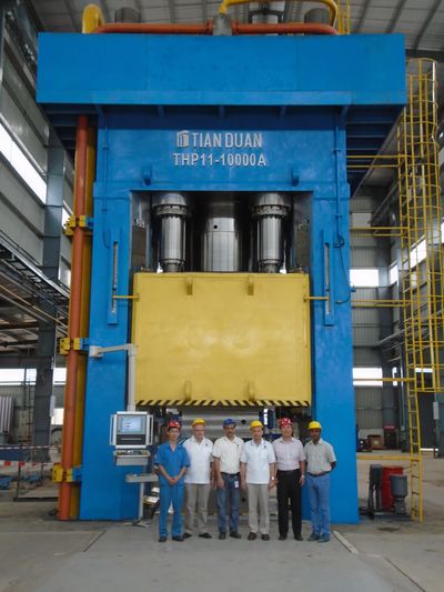 Group of workers standing in front of a large industrial press machine.