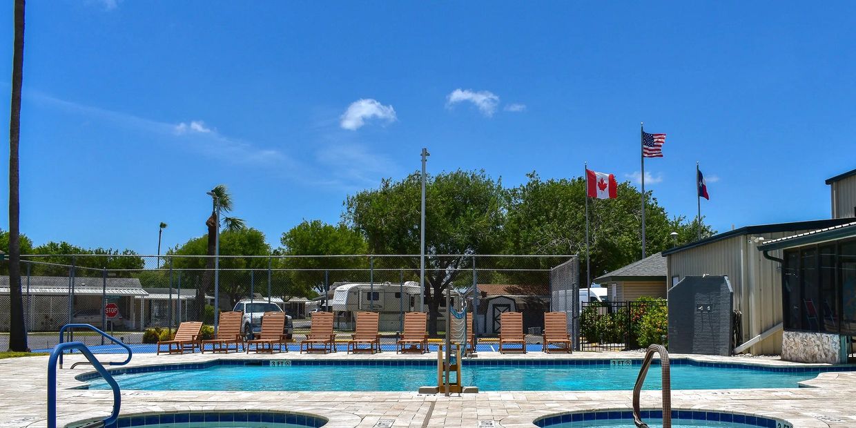 Outdoor swimming pool and hot tub with wooden lounge chairs along the deck, set against a fenced cou