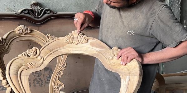 A craftsman carves intricate designs on a wooden frame.