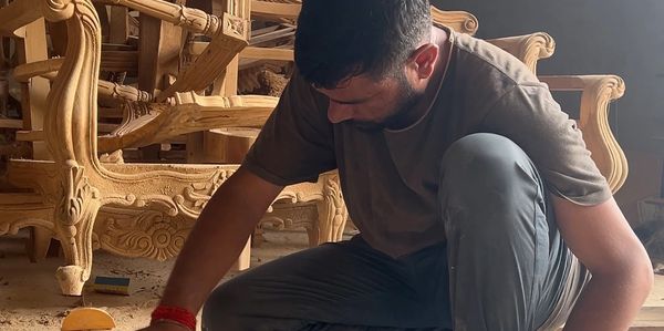 A man carving detailed designs into wooden furniture.