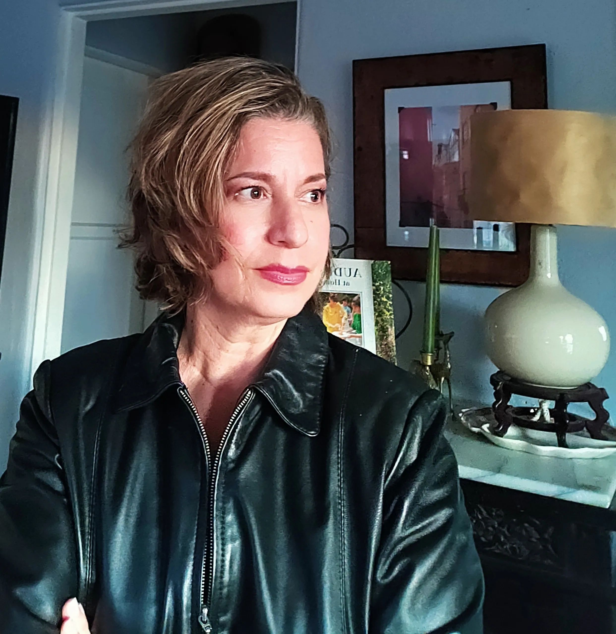 Woman in a black leather jacket looking to the side indoors.