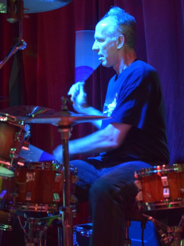 Man playing drums on stage with blue lighting.