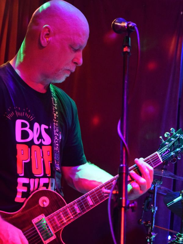 A focused musician plays electric guitar on stage with colorful lighting.