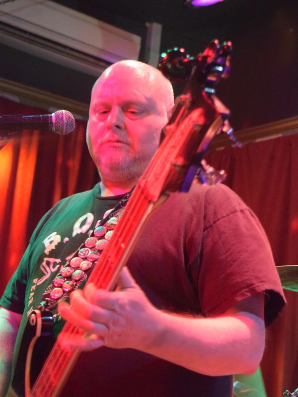 Man playing bass guitar on stage under colorful lights.