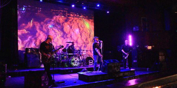 Band performing live on stage with vibrant psychedelic visuals in the background.