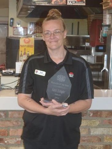Employee holding a recognition award in a pizza restaurant.