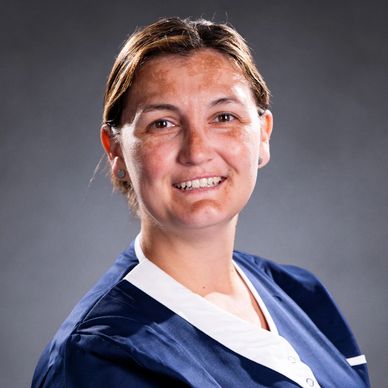 Smiling woman in a blue and white uniform against a gray background.