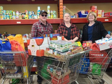 Three people with shopping carts full of groceries.