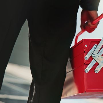 Person holding a red metal toolbox by its handle.